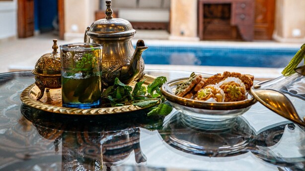Un juego de té marroquí tradicional sobre una mesa de cristal, con una piscina al fondo.