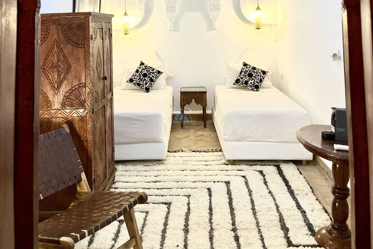 A traditional room with two beds, a chandelier, and a wooden cabinet.