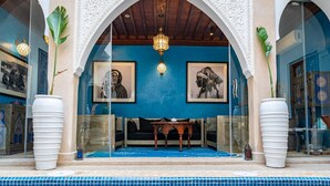 Zona de piscina interior con suelo de baldosas azules, una mesa de madera y dos grandes macetas.