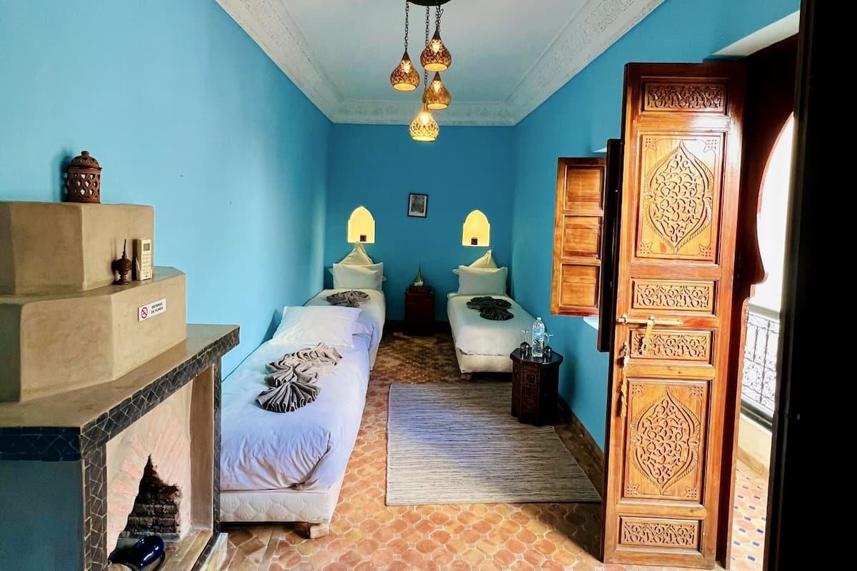 A room with two beds, a small table, a decorative door, and a patterned floor.