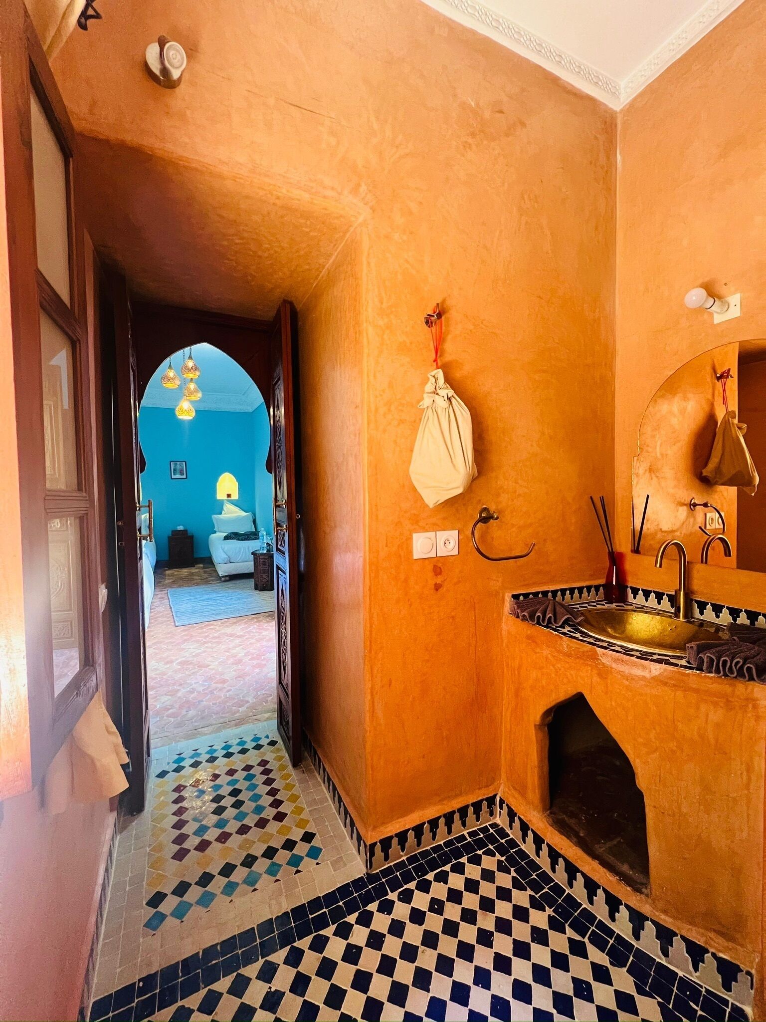 A hallway with a checkered floor, a sink with a decorative basin, and a hanging bag.