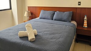 A neatly made bed with a blue quilt, two pillows, and a rolled towel.