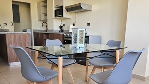 A modern kitchen with a glass dining table surrounded by four chairs, a built-in oven, and a microwave above the counter.
