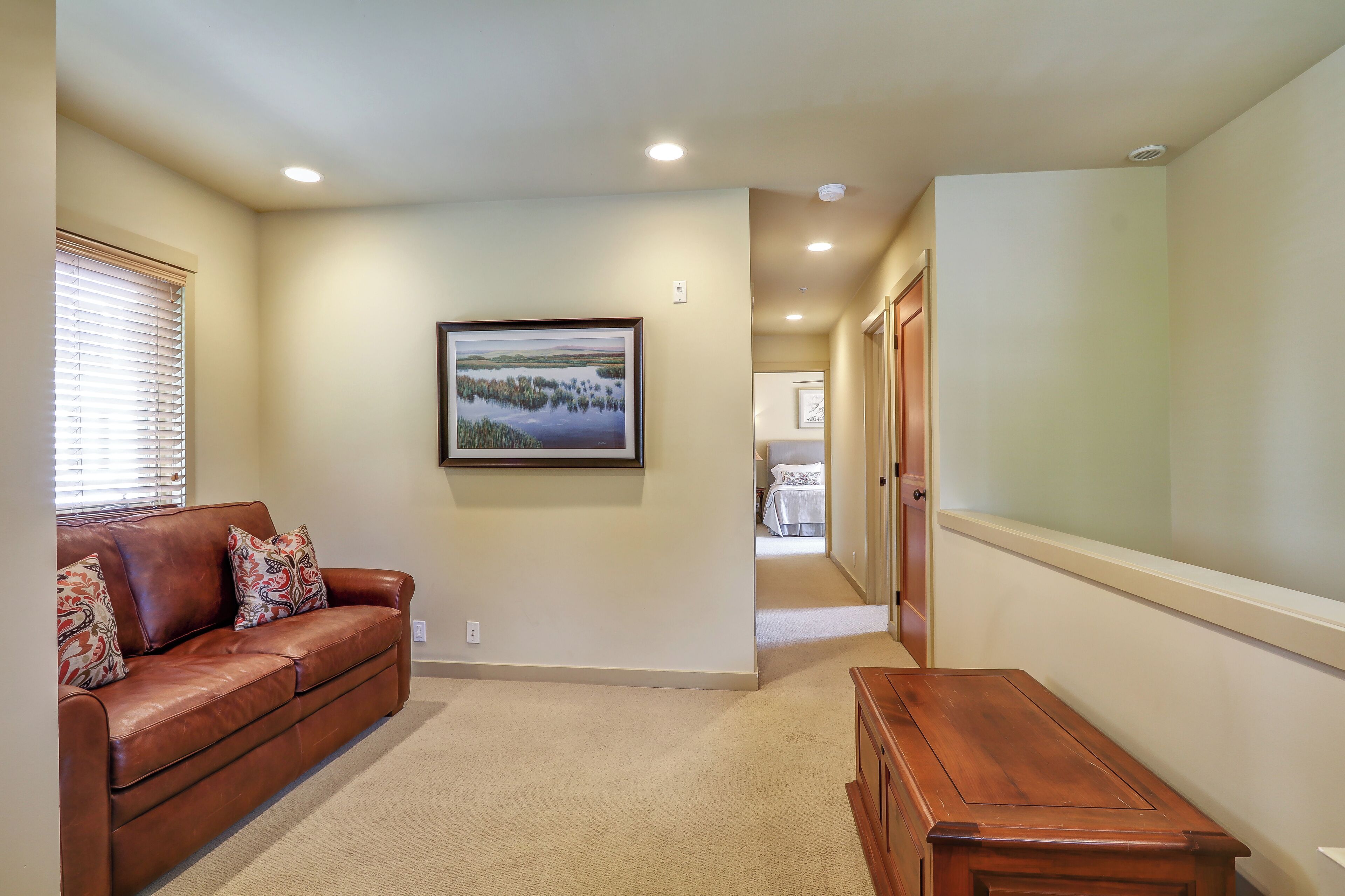 A hallway with a brown leather couch, a wooden bench, and a framed landscape painting on the wall.