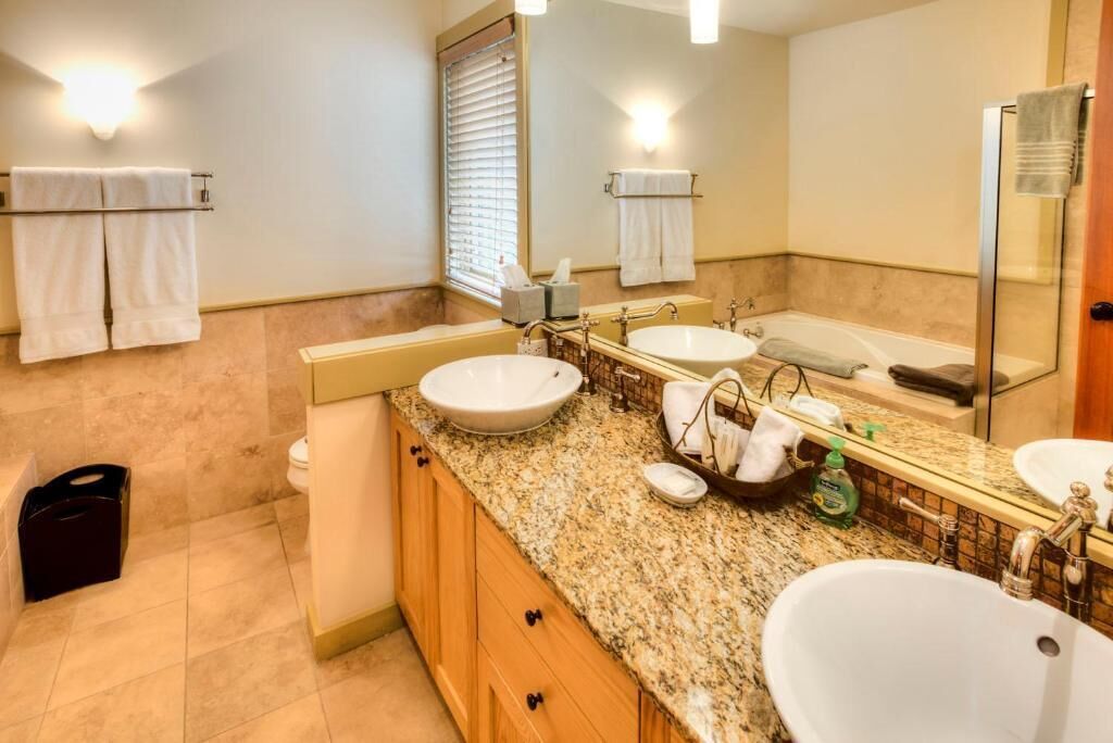 Une salle de bain avec deux lavabos, une baignoire et une douche. Des serviettes sont suspendues sur un porte-serviettes et il y a une poubelle.