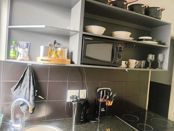 Une cuisine équipée d’un four à micro-ondes, d’étagères contenant de la vaisselle, d’une bouilloire et d’une machine à café.