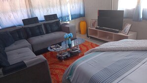 A modern living room with a sofa, a coffee table, a TV, and a bed. - Close Curtains Maboneng (Johannesburg)