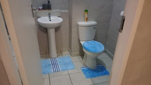 A small bathroom with a white sink, toilet, and blue mats on the floor. - Close Curtains Maboneng (Johannesburg)