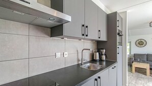 Une cuisine moderne avec des meubles de couleur grise, un évier en acier inoxydable et une machine à café posée sur le plan de travail.