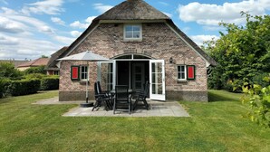 Une charmante maison en pierre avec un toit de chaume, une terrasse dotée de mobilier d’extérieur et un jardin bien entretenu.