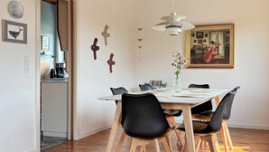 Et spiseområde med et træbord, sorte stole, en vase med blomster og et billede på væggen.