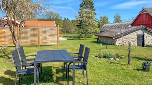 Ein Picknicktisch mit vier Stühlen auf einer Wiese, im Hintergrund ein Holzzaun und ein rotes Bauernhaus.