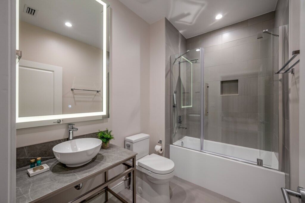 A modern bathroom with a large mirror, a white sink, a toilet, and a glass-enclosed shower area.