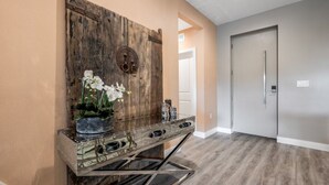 A hallway with a rustic wooden wall, a metal console table with a vase of white flowers, and a modern door. - Elegant Orlando Getaway Close to Disney (Kissimmee)