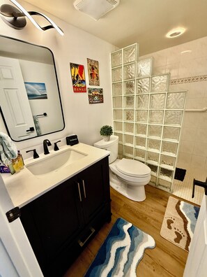 Une salle de bain avec un lavabo blanc, des meubles noirs, des toilettes et une douche à parois de verre.