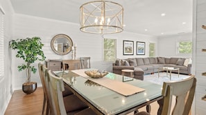 A dining area with a glass table, chairs, a chandelier, a potted plant, and a sofa in the background. - Steps to Beach & Pool Screened Porch Pelican Bay 45 at Wild Dunes Resort (Isle of Palms)