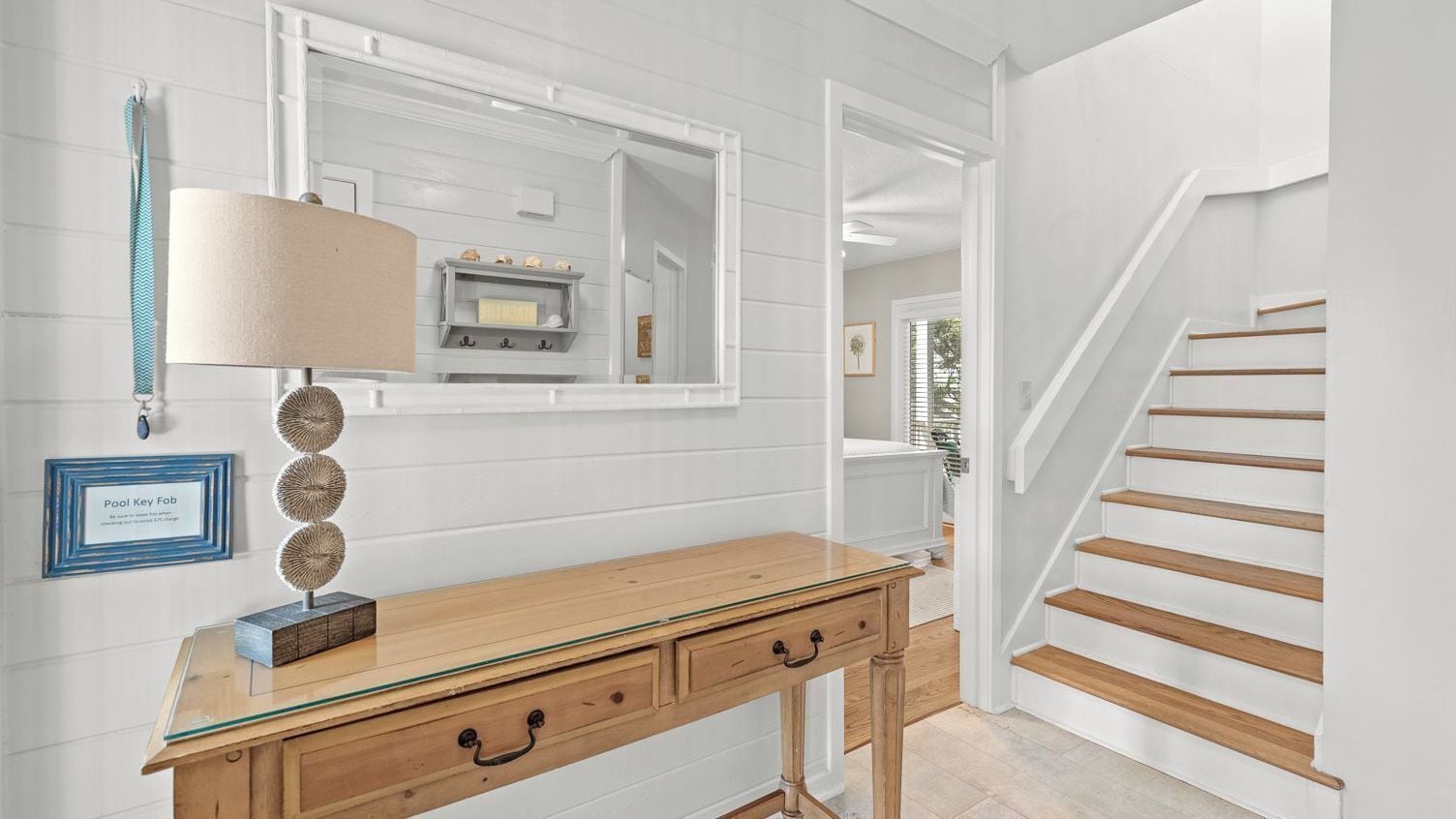 A hallway with a wooden desk, a lamp, a mirror, and a staircase.