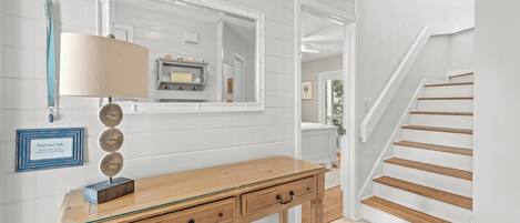 A hallway with a wooden desk, a lamp, a mirror, and a staircase.