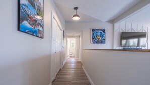 A hallway with wooden flooring, white walls, a ceiling light, and artwork.