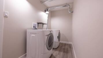 A laundry room with two front-loading washing machines, a light fixture, and a vent pipe on the ceiling.
