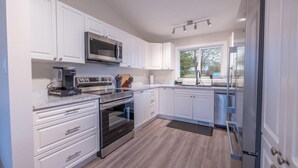 A modern kitchen with white cabinetry, stainless steel appliances, and a large window providing natural light.