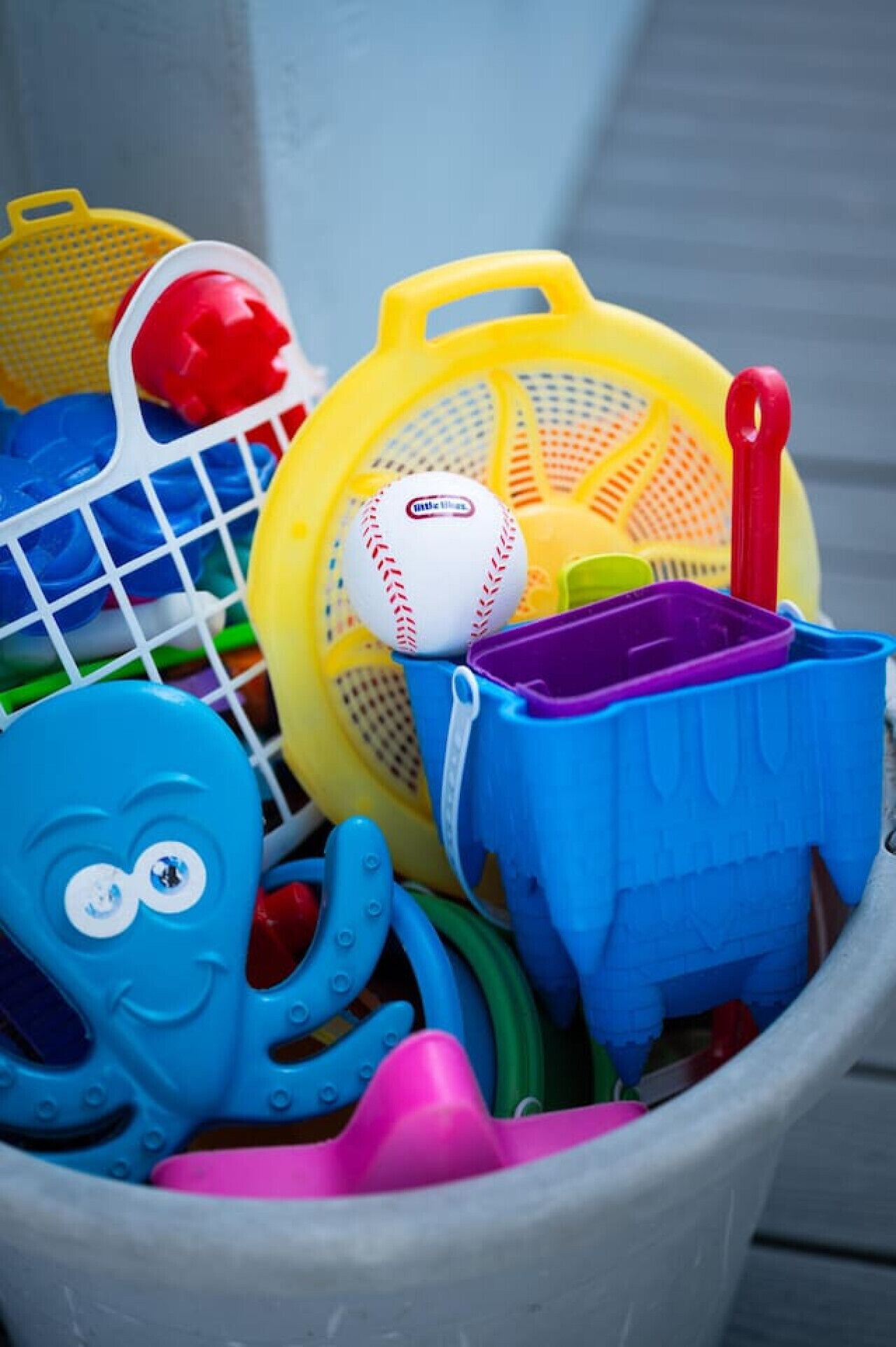 Un seau rempli de divers jouets en plastique de couleurs vives et une balle de baseball blanche.