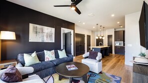 A modern living room with a sofa, armchairs, a coffee table, and a kitchen area with a sink and microwave.