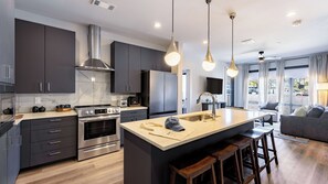 A modern kitchen with dark cabinetry, stainless steel appliances, and a central island with stools.