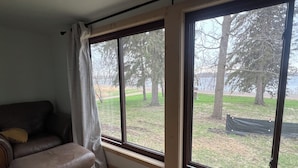 A room with a large window, a leather sofa, and a view of a grassy area with trees.