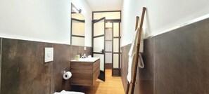 A narrow bathroom with a wooden vanity, a toilet paper holder, and a mirror. - Near CityLife & Thermal Baths – Spacious apartment with 2 baths and XL living (Milano)