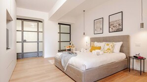 Ein modernes Schlafzimmer mit einem großen Bett, einem Nachttisch und einem kleinen Tisch mit einer Lampe.