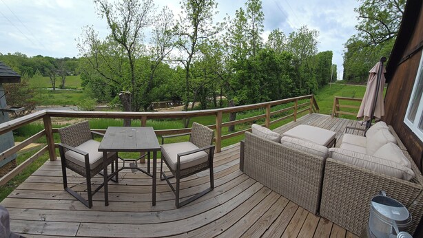 A wooden deck with a table and chairs, a wicker sofa, and a wooden railing.