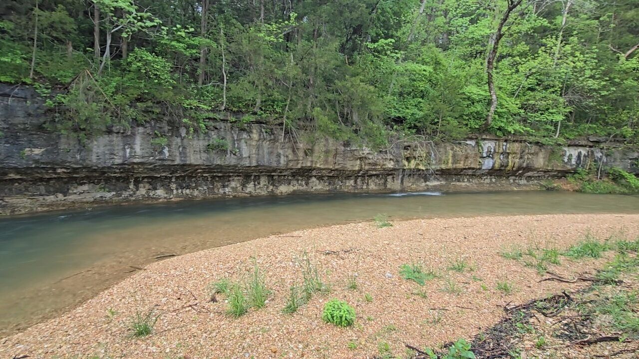 Ein Fluss mit steiler Uferböschung und kiesigem Vordergrund.
