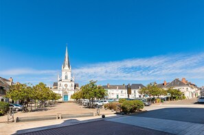 Een kerk met een hoge punt, omgeven door bomen en geparkeerde auto's op een stadsplein.