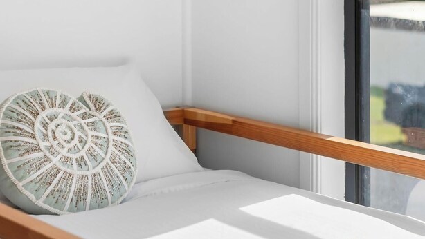 Una habitación iluminada por el sol con una silla blanca acolchada y un cojín decorativo.