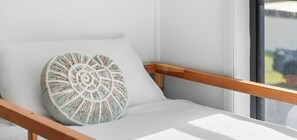 A sunlit room with a white cushioned chair and a decorative pillow.