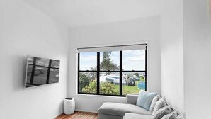 Una habitación con un ventanal amplio, un televisor de pantalla plana en la pared, un sofá gris y un jarrón blanco sobre el suelo.