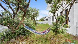 Una hamaca entre árboles en un patio trasero con una valla blanca y una casa al fondo.