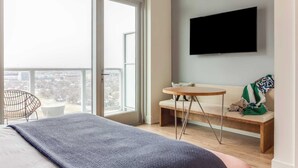 A modern bedroom with a large window, a bed, a sofa, a small table, and a TV mounted on the wall. - Luxe High Rise Near DT Austin w/ Views Rooftop Pool, Gym, & Luxe Amenities (Austin)