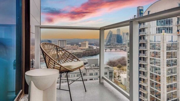 A balcony with a view of a cityscape, a wicker chair, and a white table. - Luxe High Rise Near DT Austin w/ Views Rooftop Pool, Gym, & Luxe Amenities (Austin)
