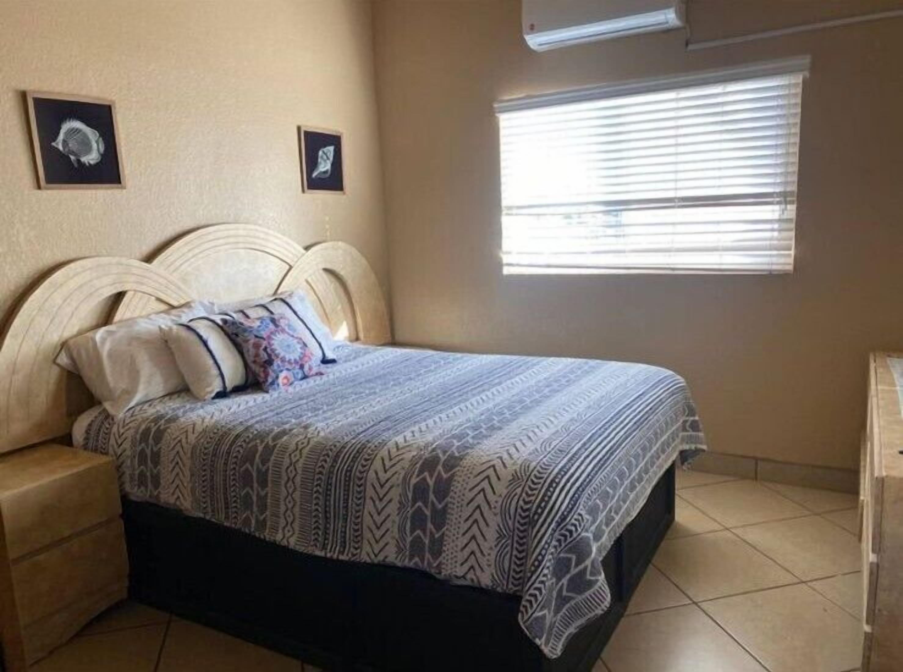A bedroom with a bed, a nightstand, a window with blinds, and two framed pictures on the wall.