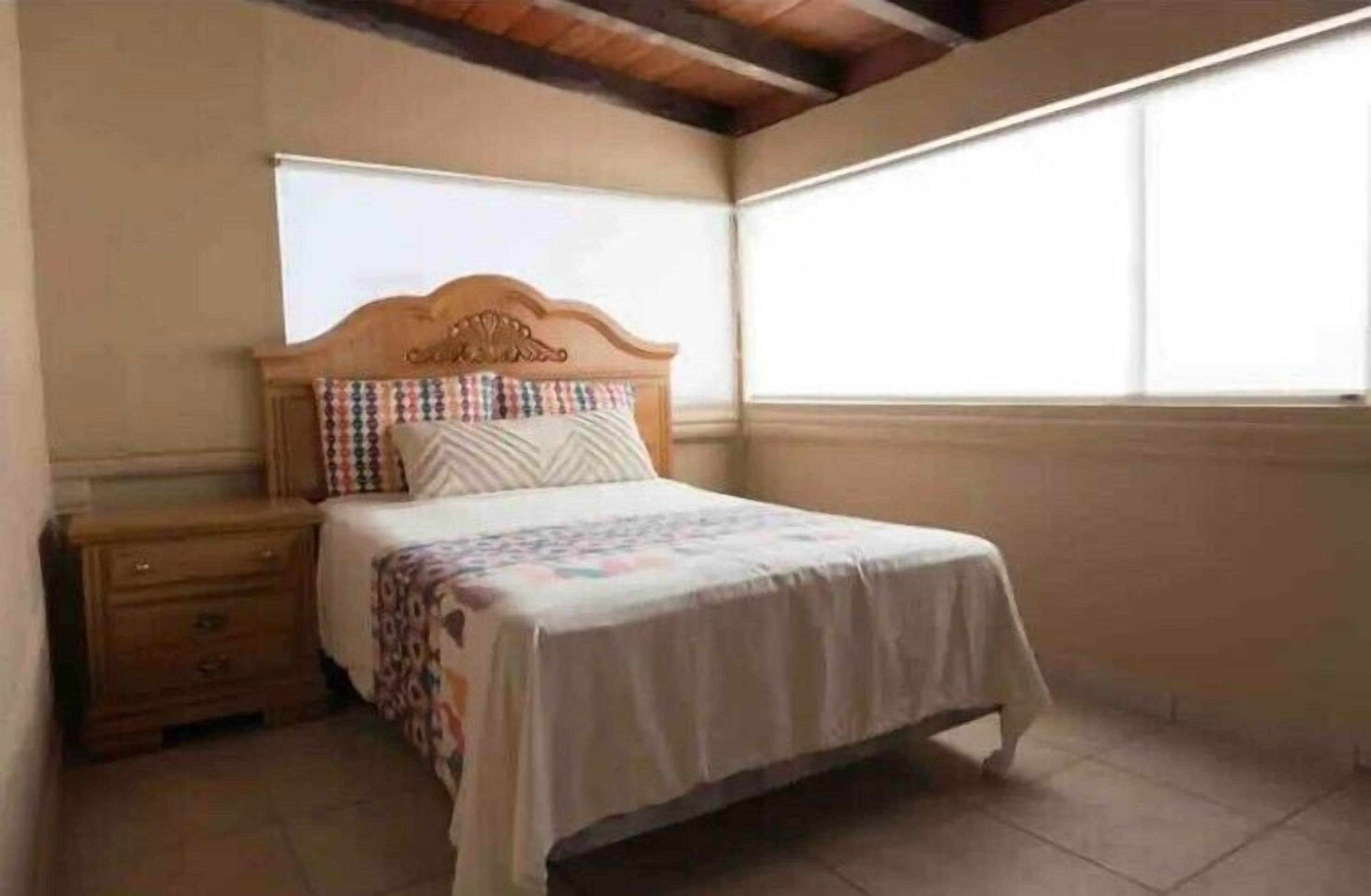 A bedroom with a wooden bed, a nightstand, a window with blinds, and a tiled floor.