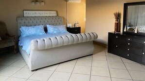Une chambre à coucher avec un grand lit, une table de chevet, une commode et un climatiseur fixé au mur.