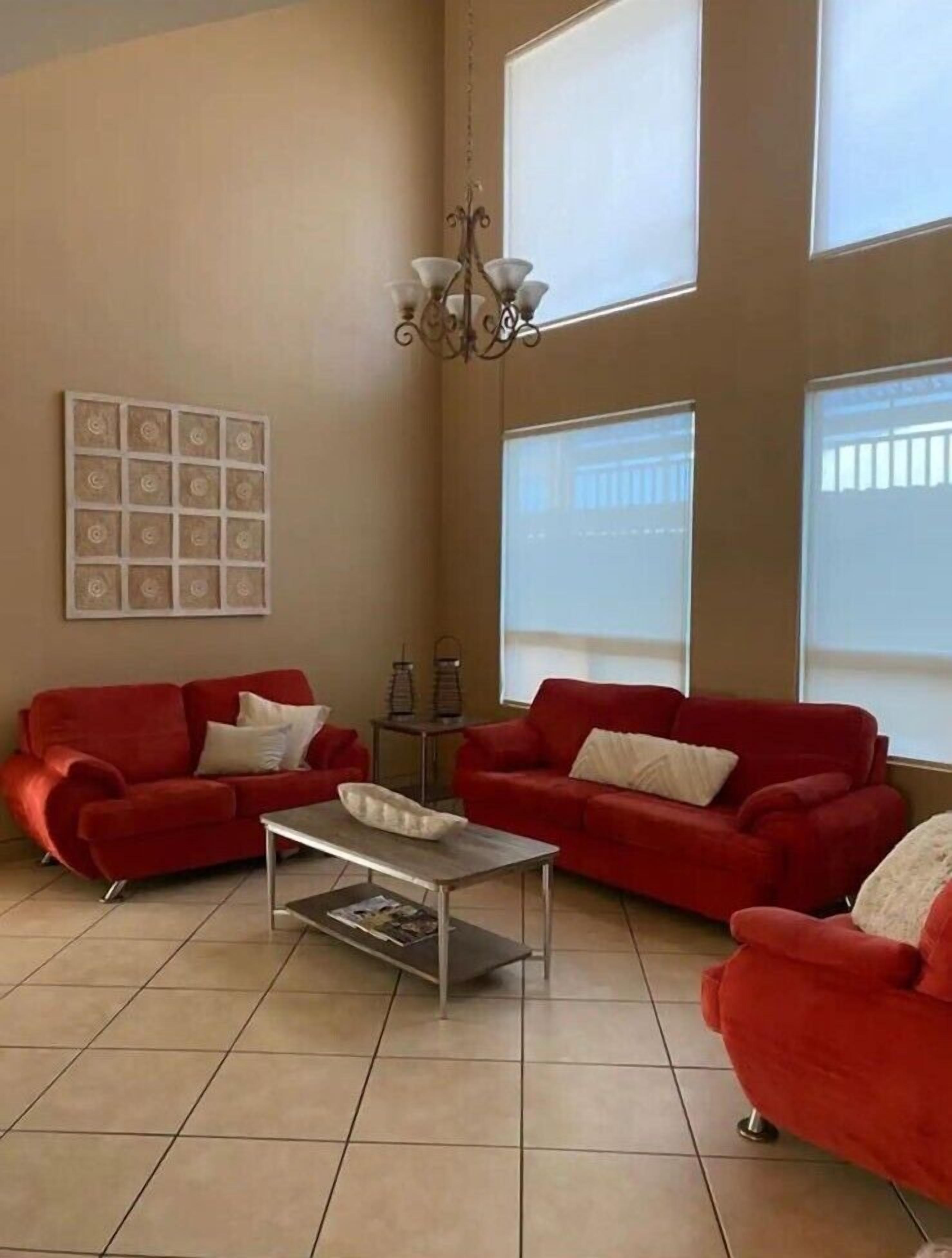 A spacious living room with two red sofas, a coffee table, and a chandelier.