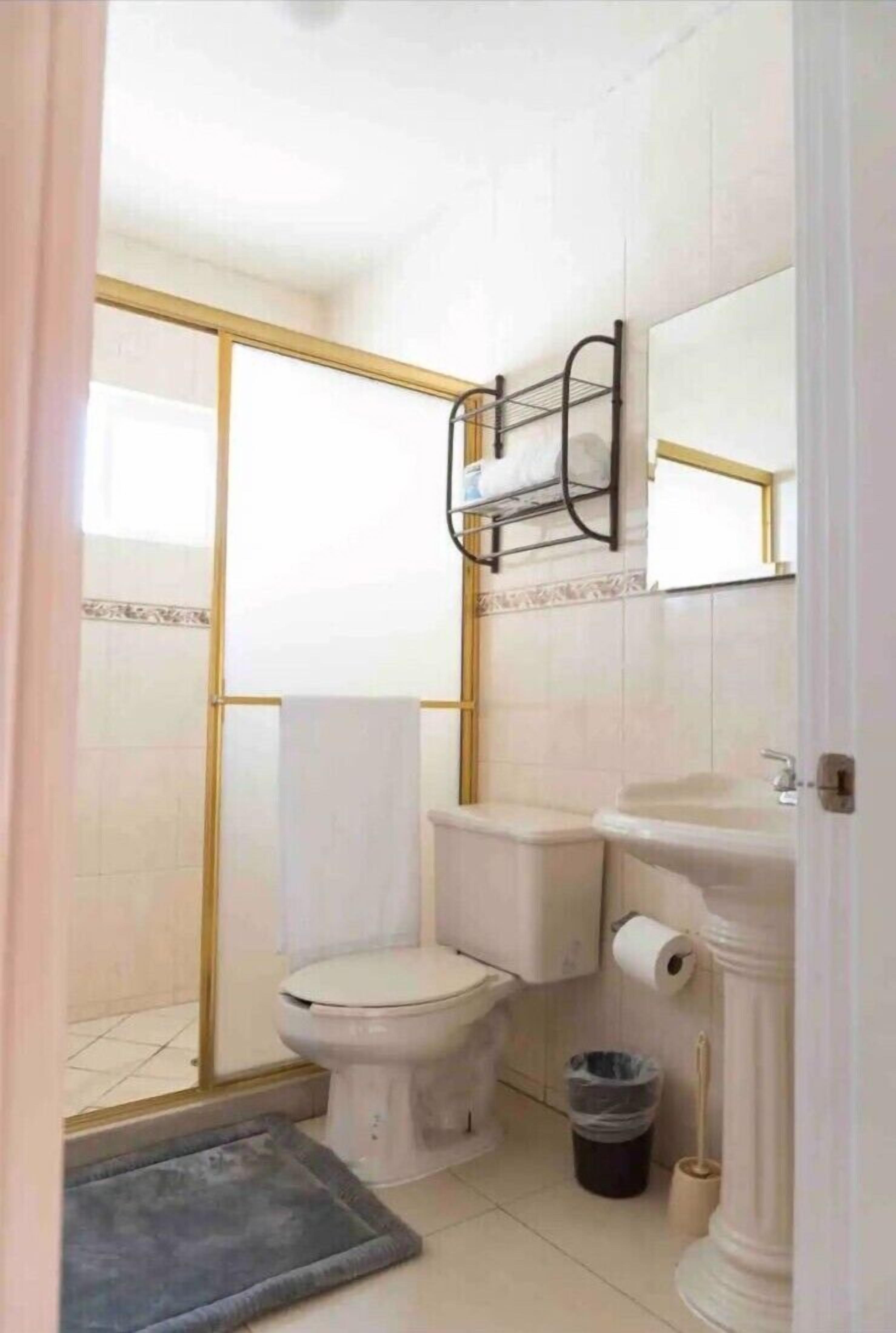 A bathroom with a toilet, bidet, and sink. There is a shower area with a glass door and a towel rack above the sink.
