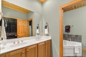 A bathroom with a double sink, wooden cabinets, a bathtub, and a mirror.