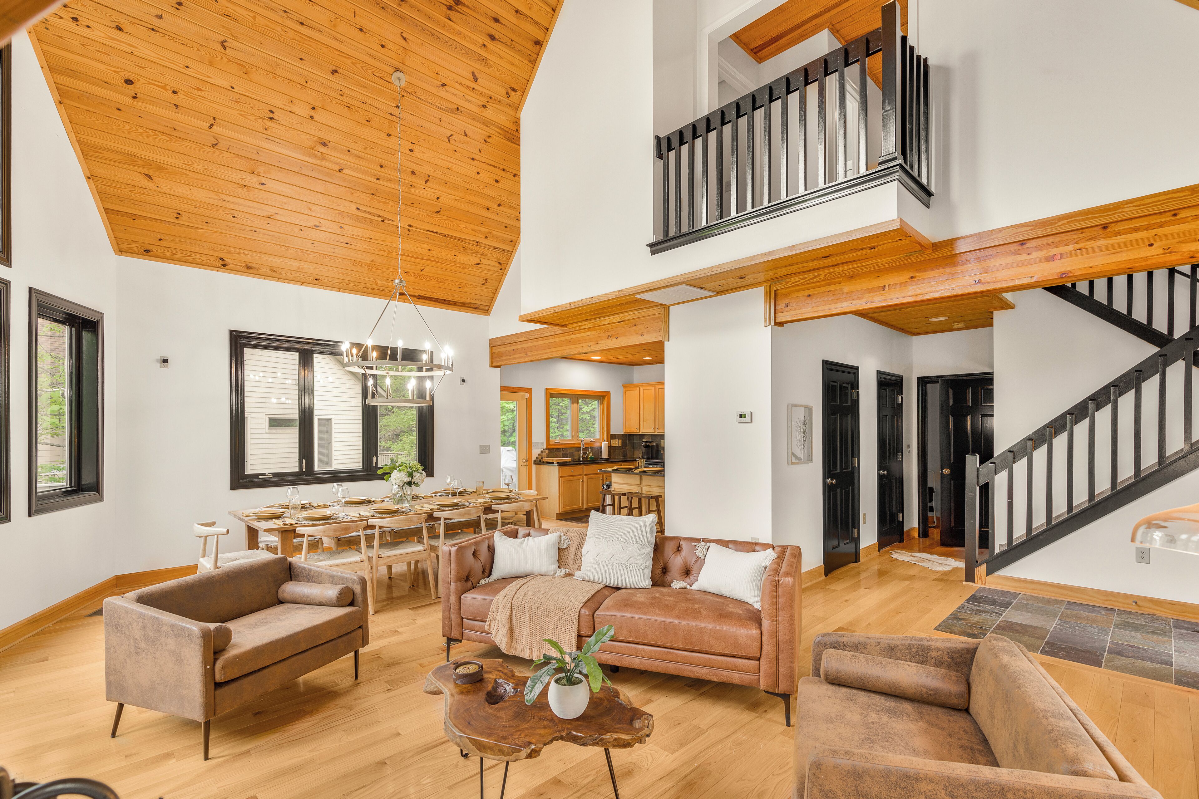 A spacious living area with a high ceiling, wooden beams, a dining area, and a staircase leading to an upper level.