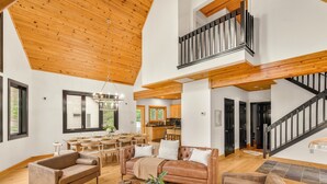 Un vaste espace de vie doté d’un plafond haut, de poutres apparentes, d’un coin repas et d’un escalier menant à un niveau supérieur.