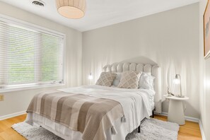 A bedroom with a bed, bedside table, lamp, and window with blinds.
