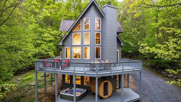 Une maison à deux étages avec un balcon, un jacuzzi et un tonneau en bois.